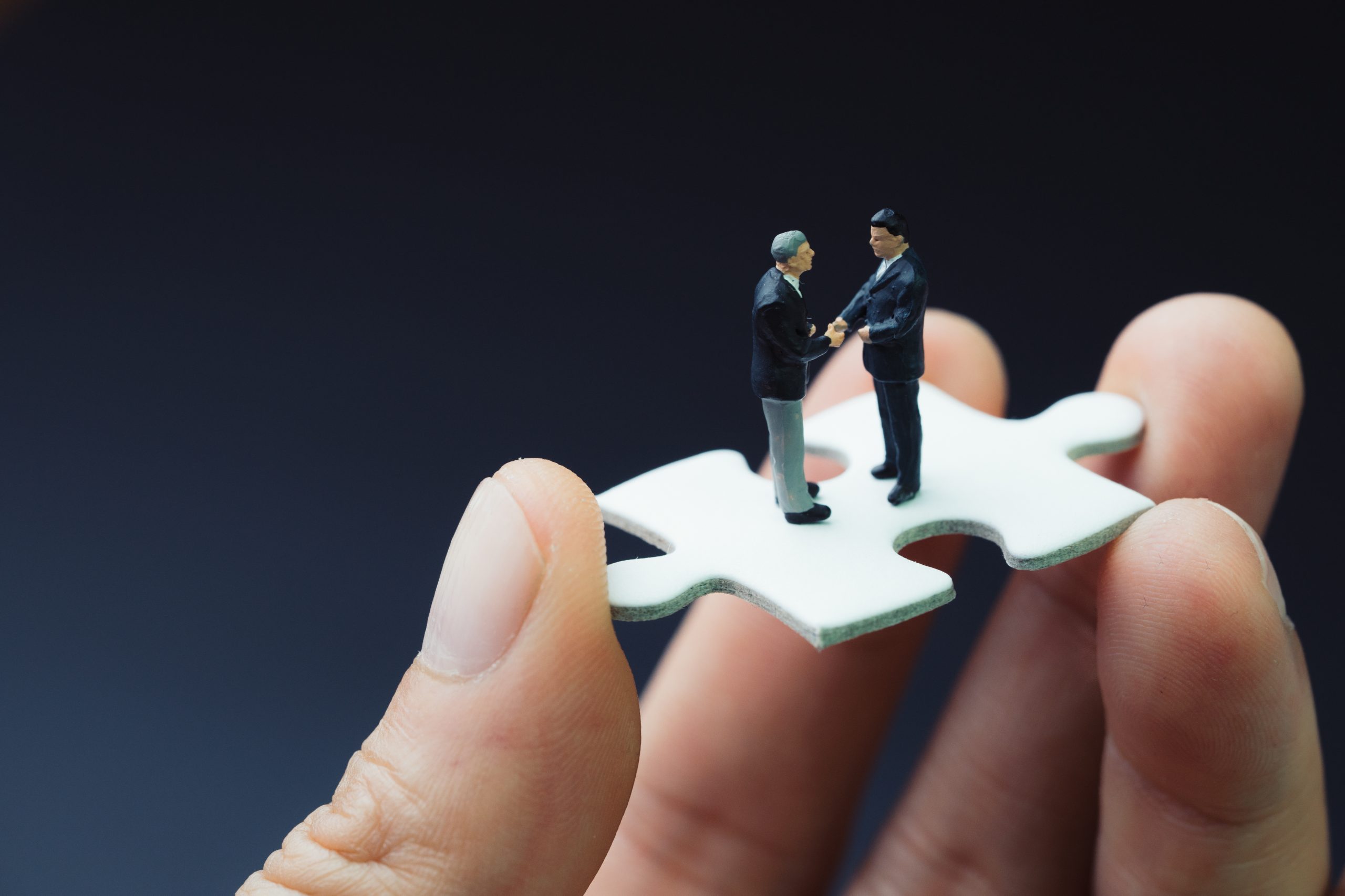 Two miniature figures standing on a puzzle piece held by human fingers, symbolizing collaboration and problem-solving in legal disputes.
