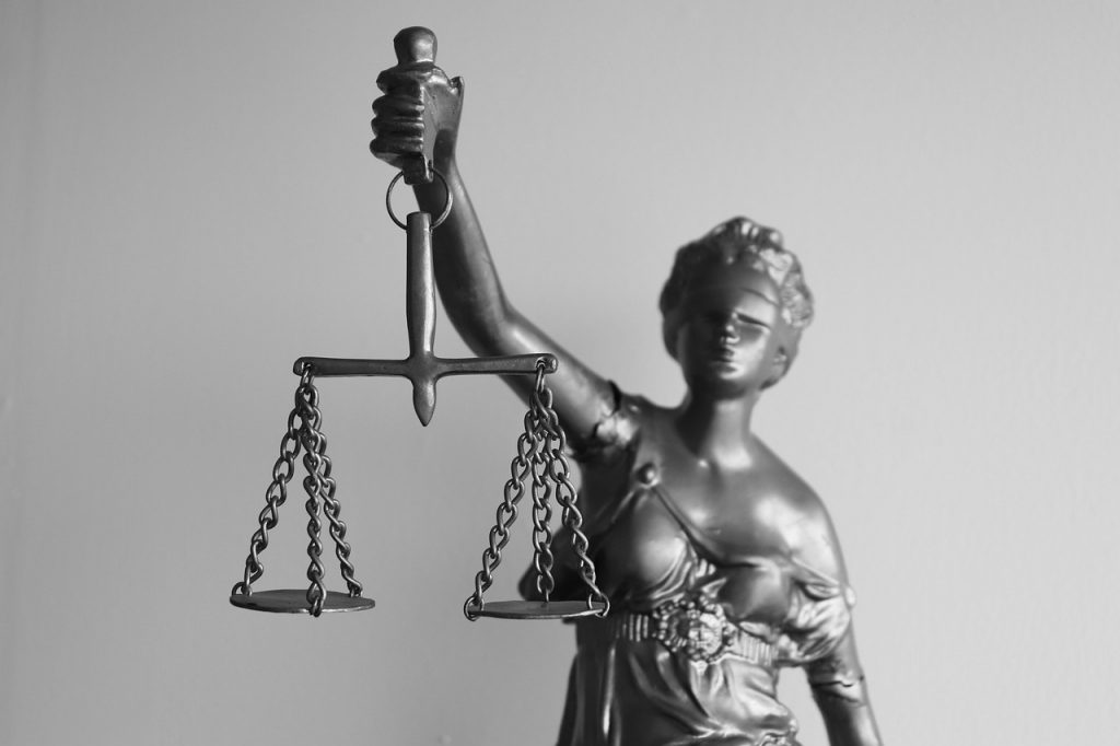 Black and white image depicting a statue of Lady Justice, holding a set of scales in her right hand. The statue is partially visible, emphasizing the scales and the blindfolded figure, symbolizing impartiality and client advocacy.