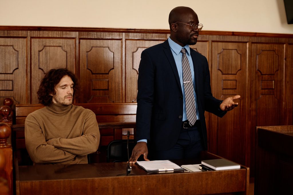 Confident African American male attorney in formalwear explaining points of case to judge while standing next to suspect during trial session