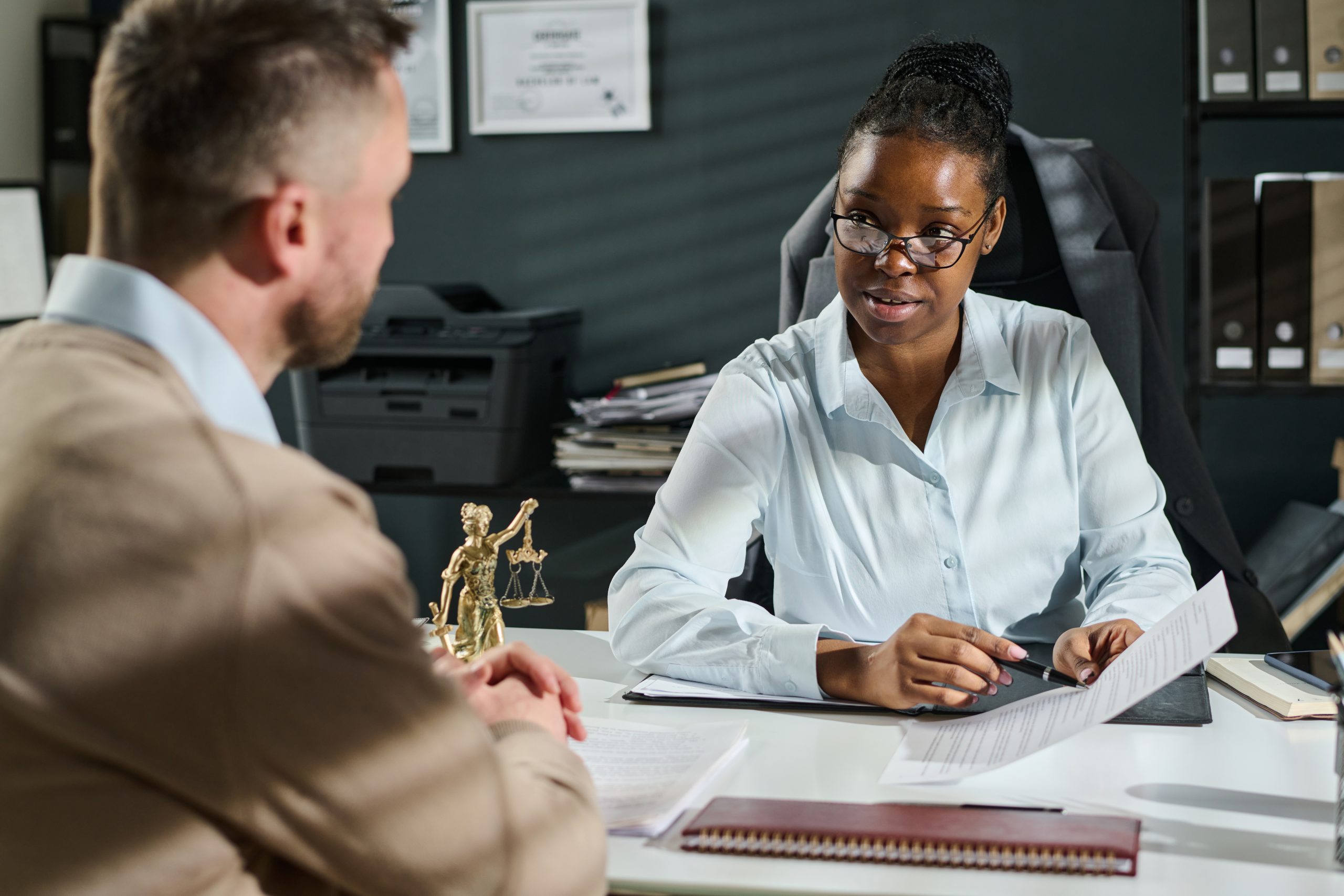 Young confident female lawyer or notary looking at male client while explaining him points of business contract or other document