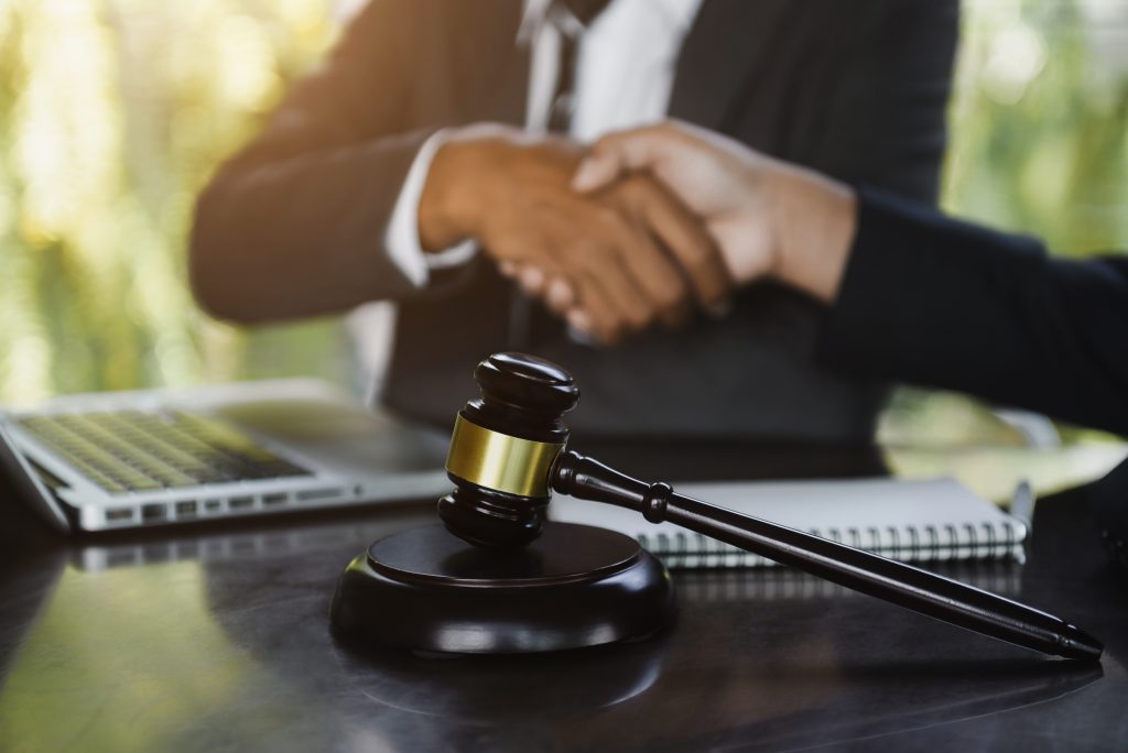 Two individuals are shaking hands over a desk with a gavel, a notebook, and a laptop in the foreground. The setting appears to be a professional office environment in Florida, possibly related to legal or business matters, such as an expungement procedure.