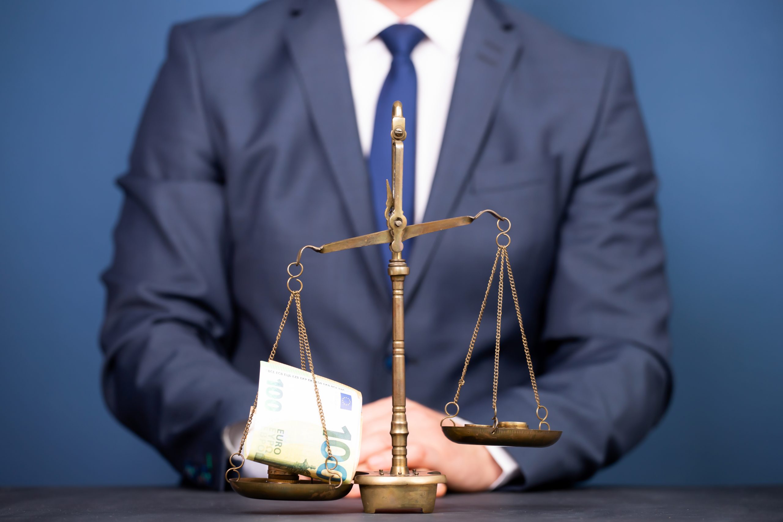 A person in a suit sits behind a balance scale. One side holds several 100 euro bills, while the other side is empty, symbolizing the essential guide to understanding money’s worth beyond currency. The solid blue background adds depth to this compelling concept.