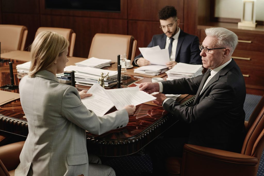 Senior lawyer passing paper to his female colleague, middle eastern man reading papers on background