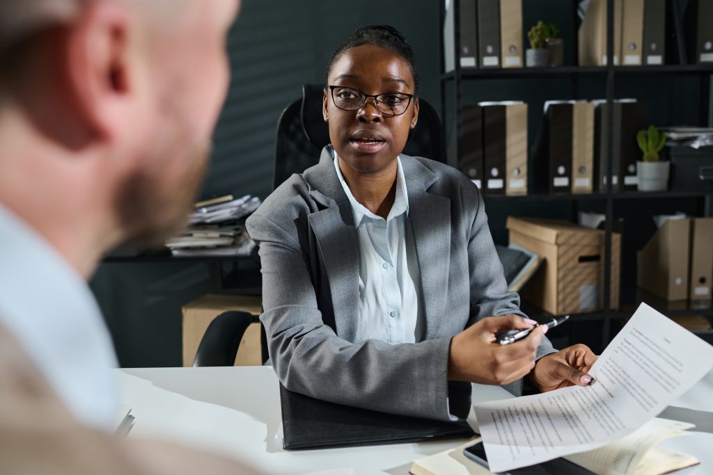 Young confident lawyer or solicitor sitting in front of male client and looking at him while explaining points of business contract