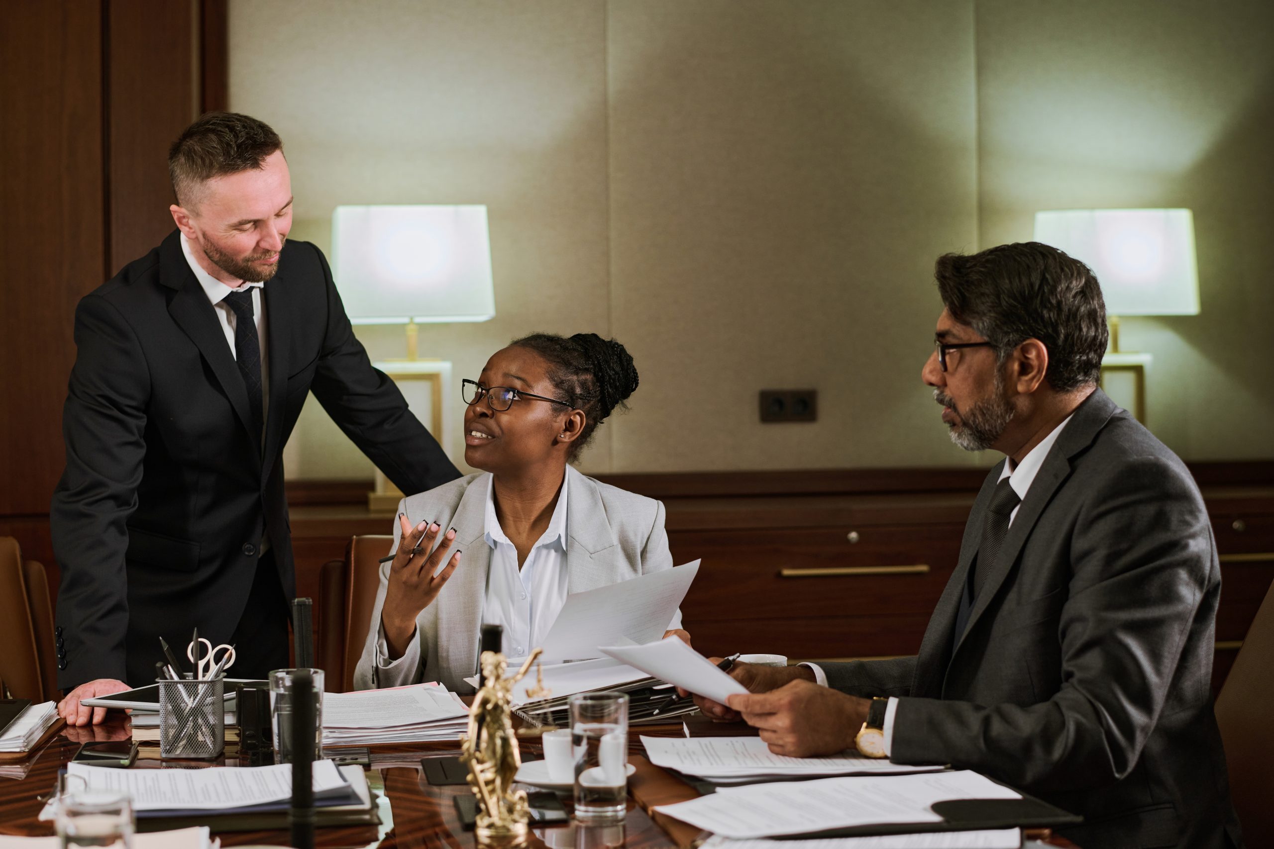 Young confident African American businesswoman looking at one of two male colleagues during discussion of main points of document